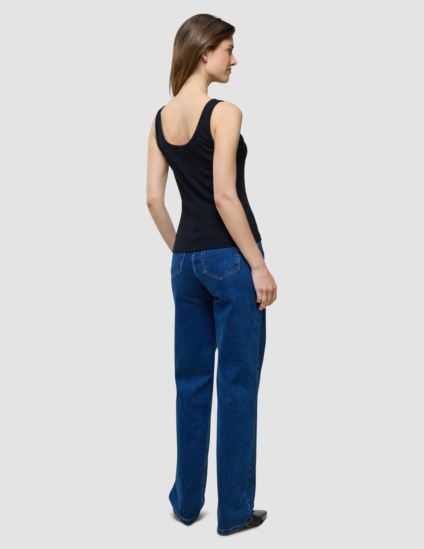 Eine Frau, von hinten gesehen, die ein schwarzes Rib-Tanktop und eine blaue Jeans trägt.